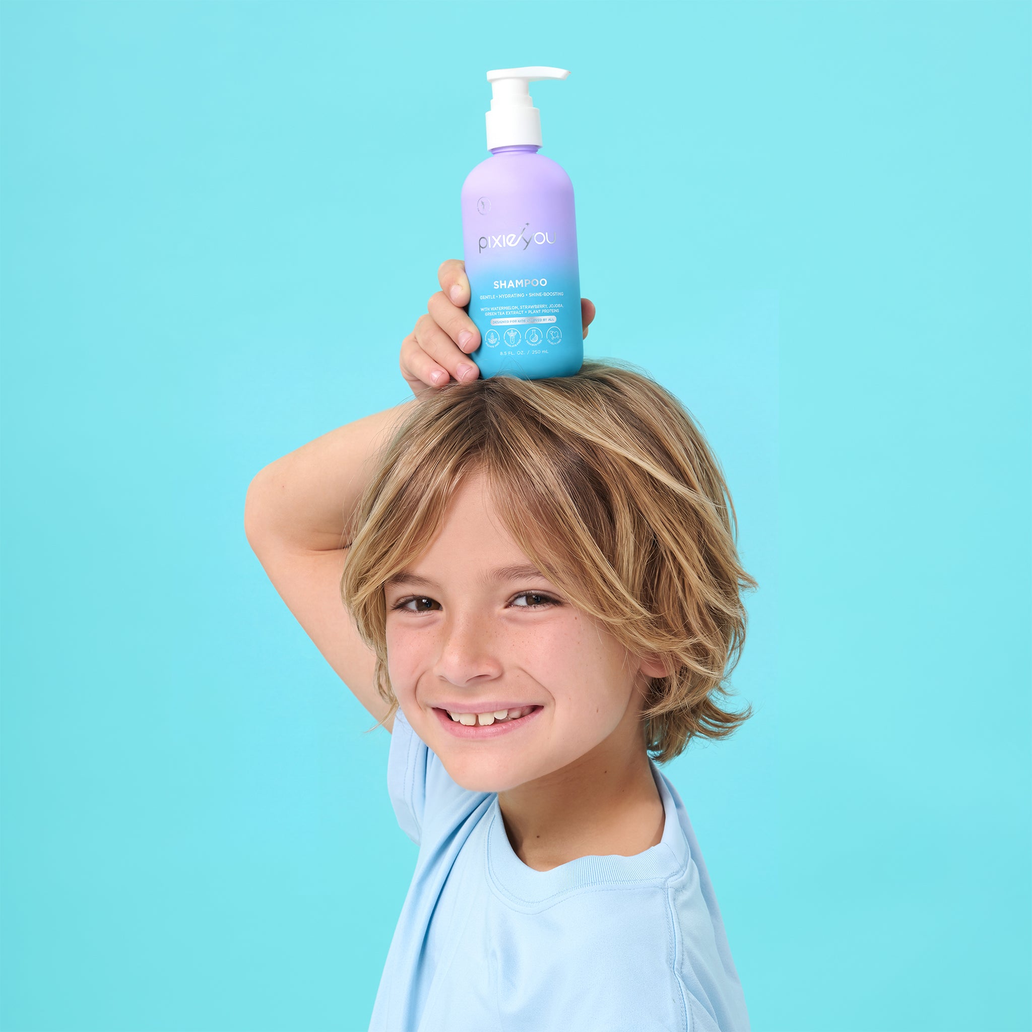 PixieYou shampoo bottle held by a smiling child against a bright blue background.