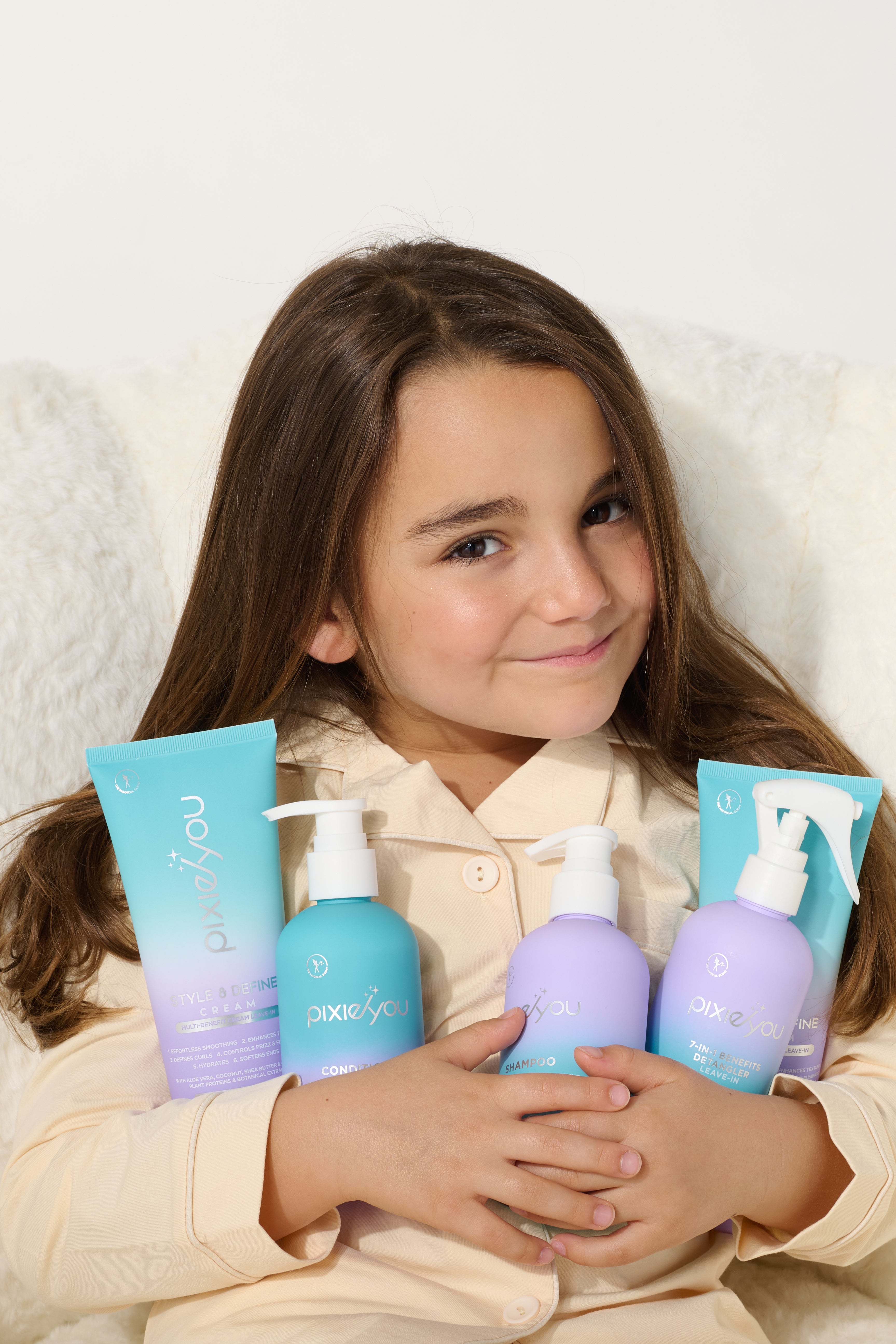 A young girl smiles while holding PixieYou's Starter Set, featuring colorful hair care products in blue and purple bottles.