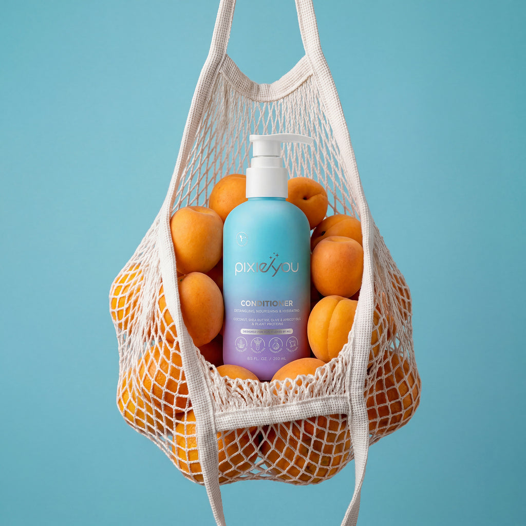 PixieYou Conditioner in a blue bottle, nestled among fresh apricots in a mesh bag against a light blue background.