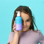 PixieYou Conditioner in a blue and purple bottle held by a girl against a bright blue background.